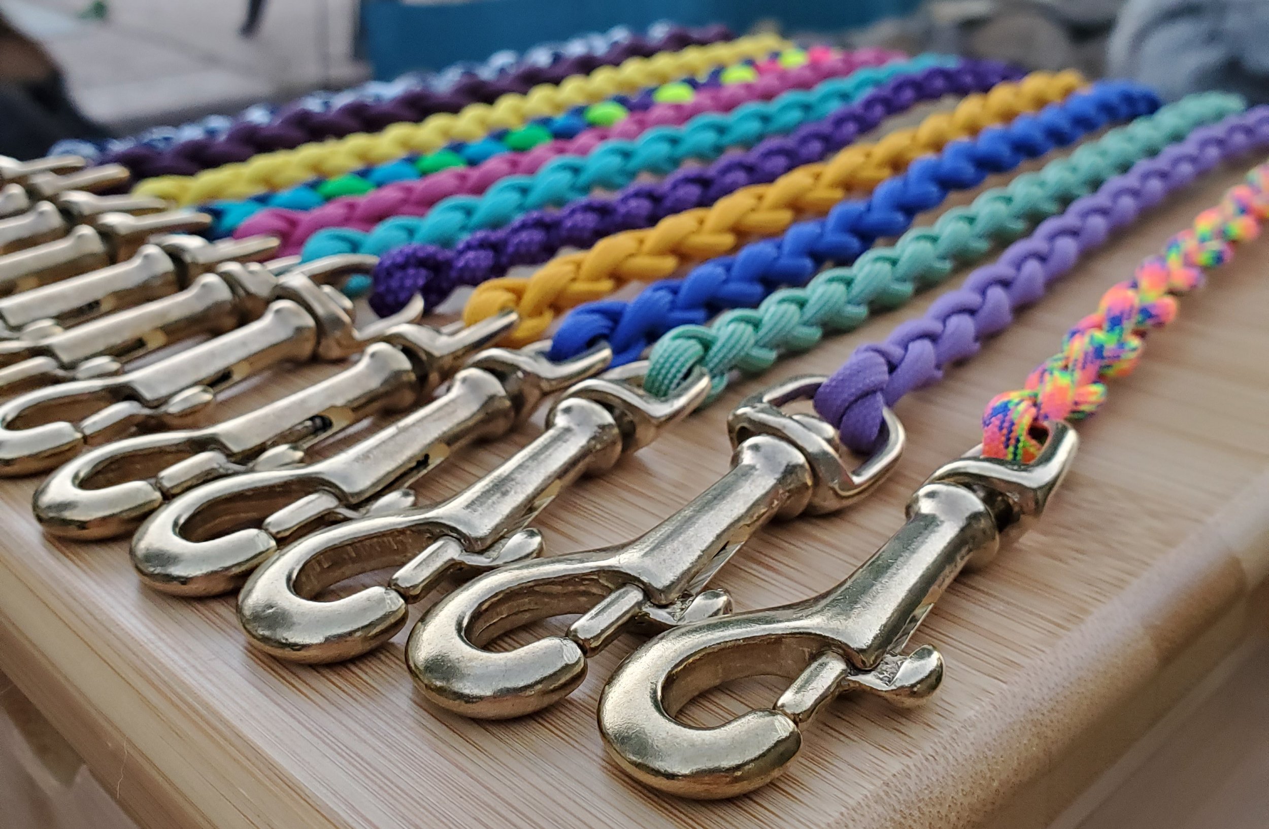 Rows of colorful braided bracelets with metal clasp hooks on a wooden surface.