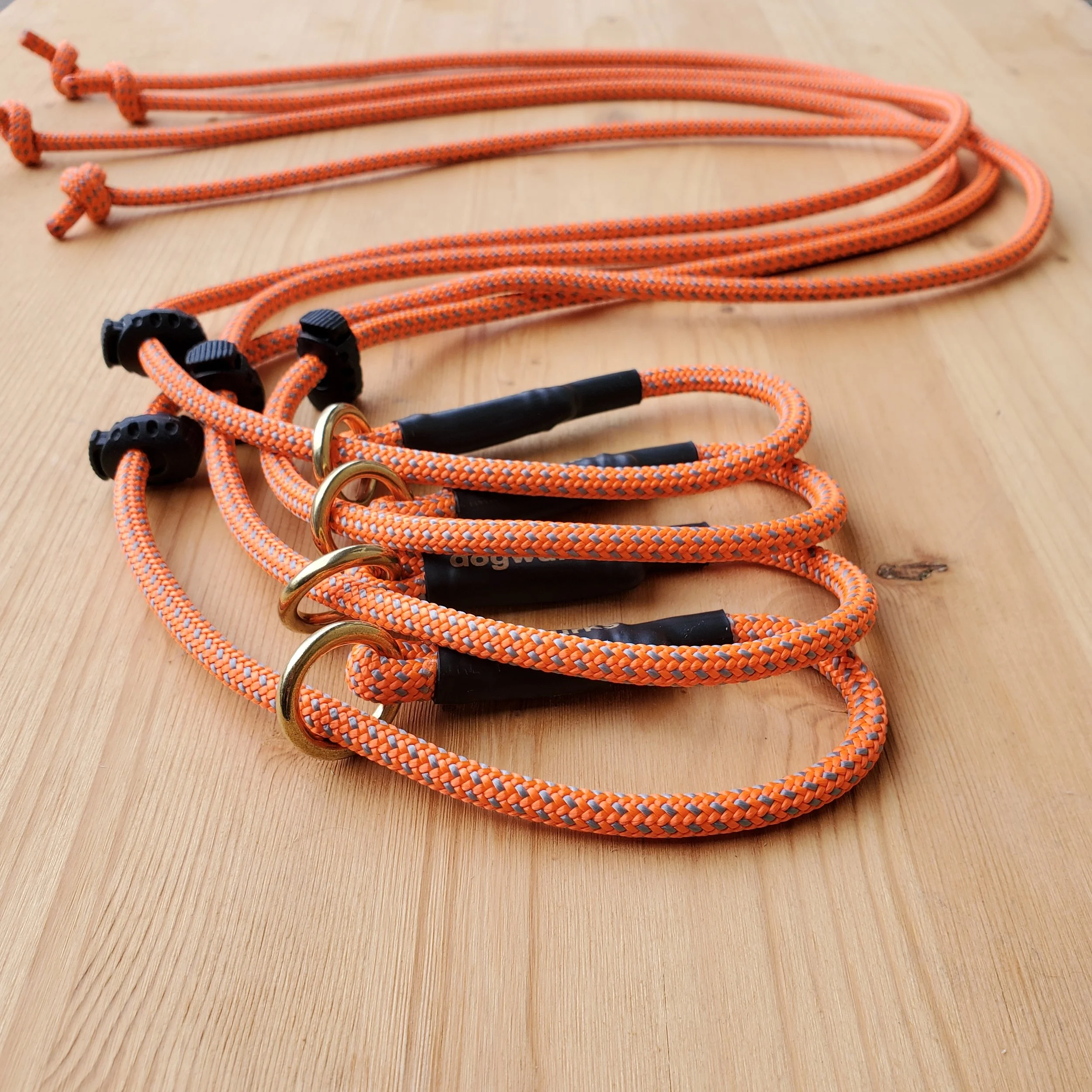 Four orange and blue braided climbing ropes with black and gold metal clips lying on a wooden surface.