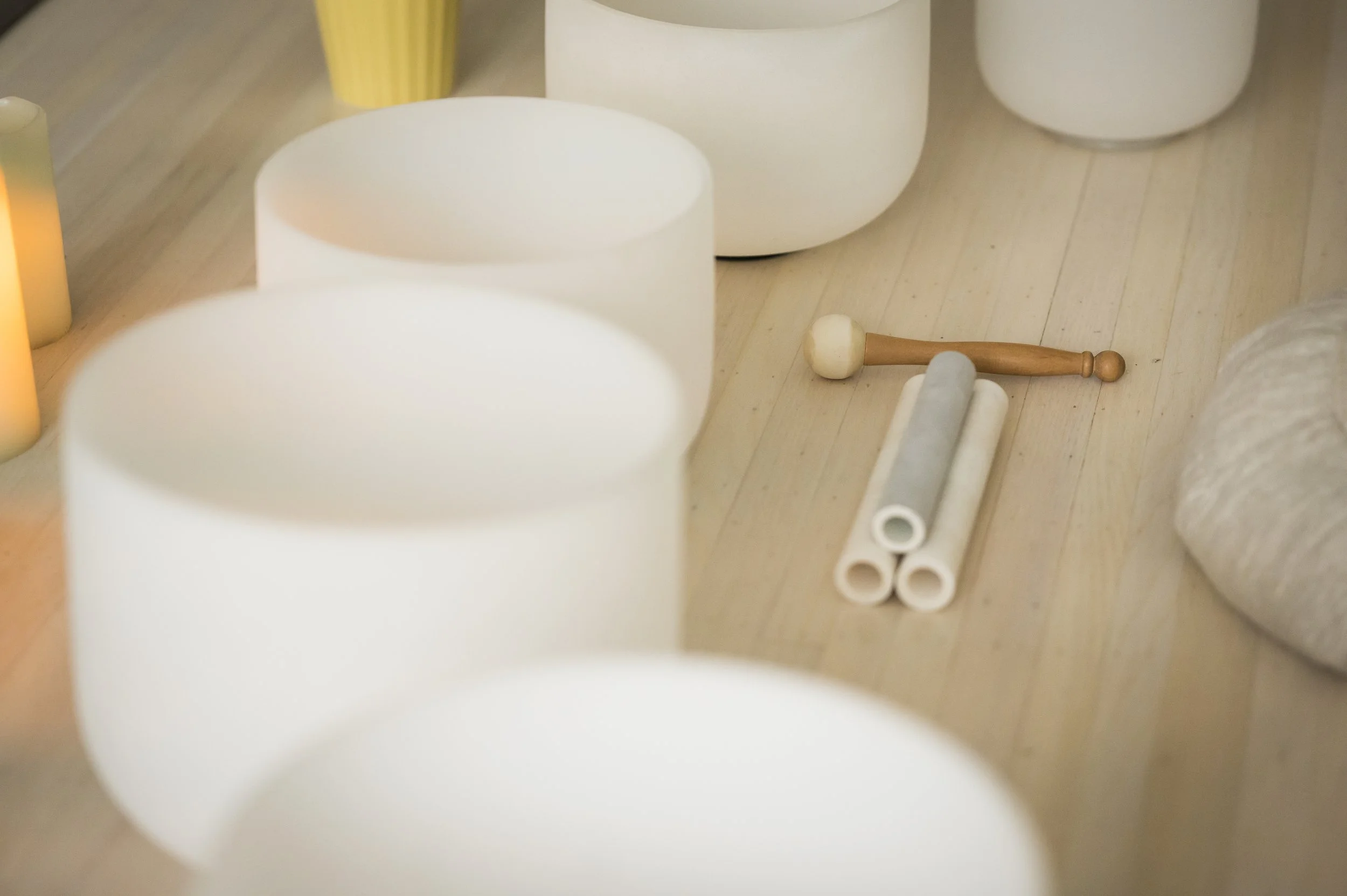 Close-up of white cylindrical candles, a wooden mallet, and a gray rolling pin on a light wooden surface.