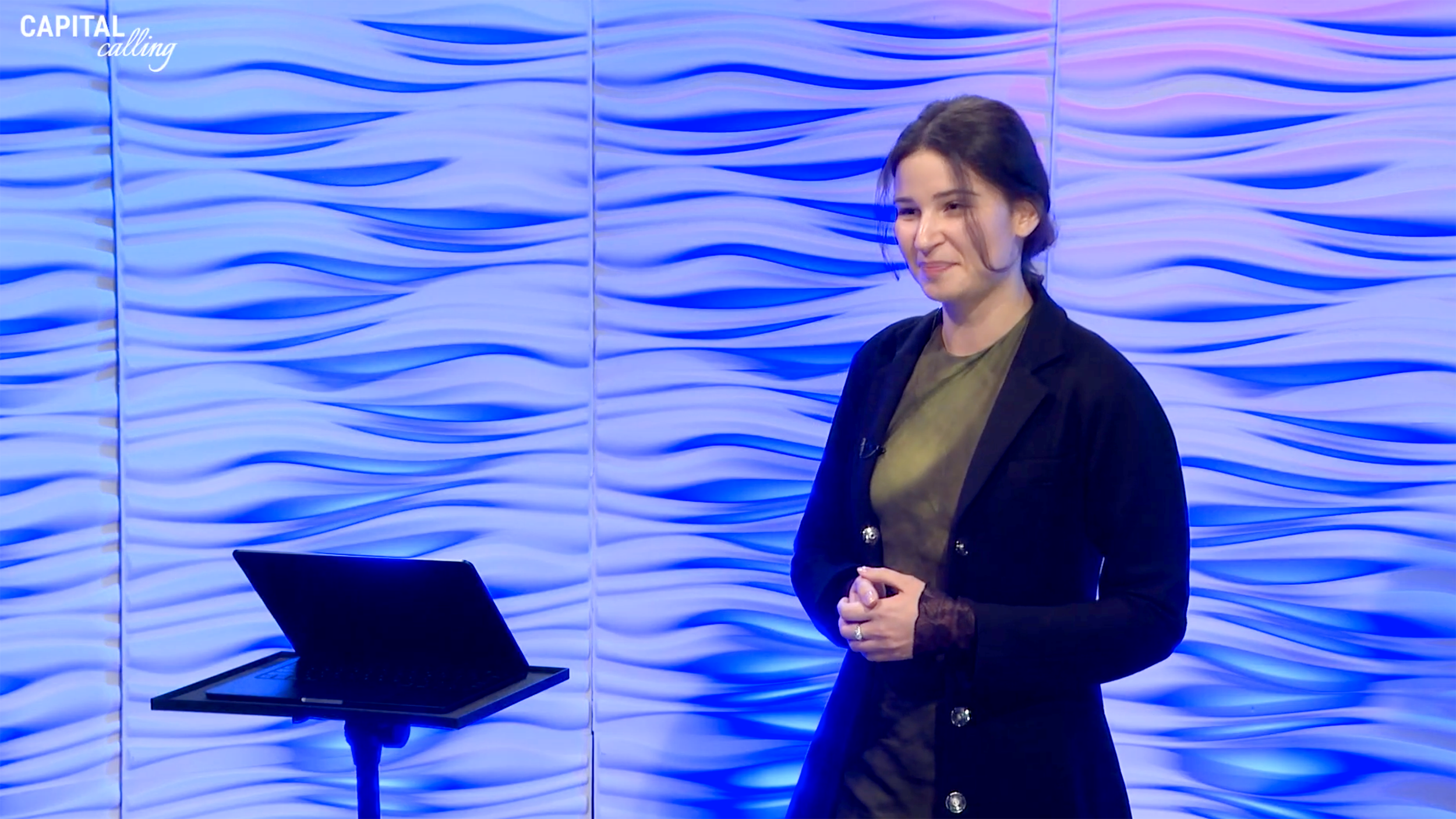 Young woman smiling at people off-camera. A laptop is in front of her on a stand.