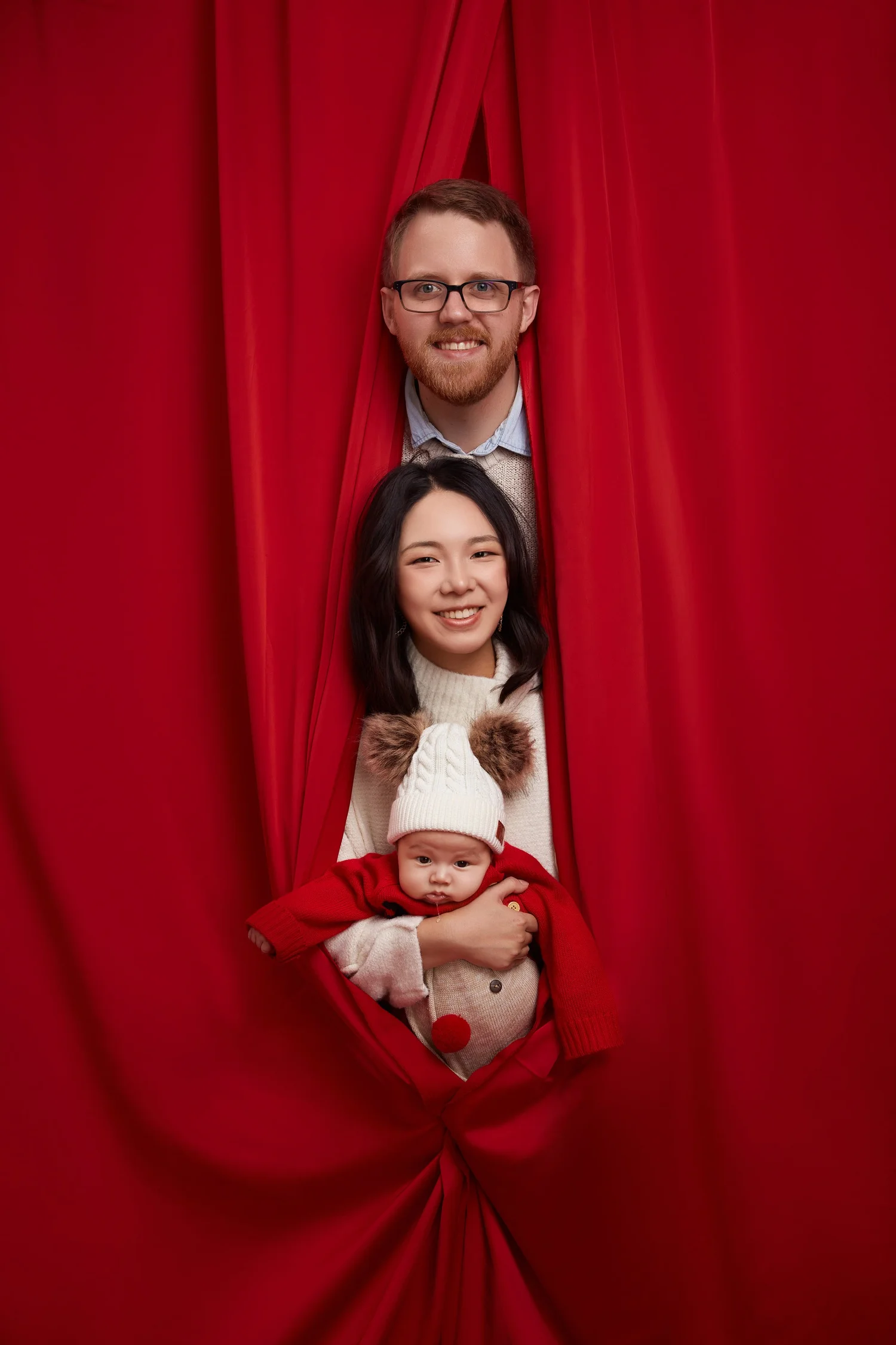 Family framed by a draped red velvet curtain, baby in red