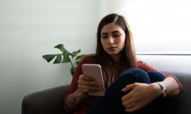 Frau schaut auf ihr Handy und wartet auf eine Nachricht von einem emotional unverfügbaren Mann
