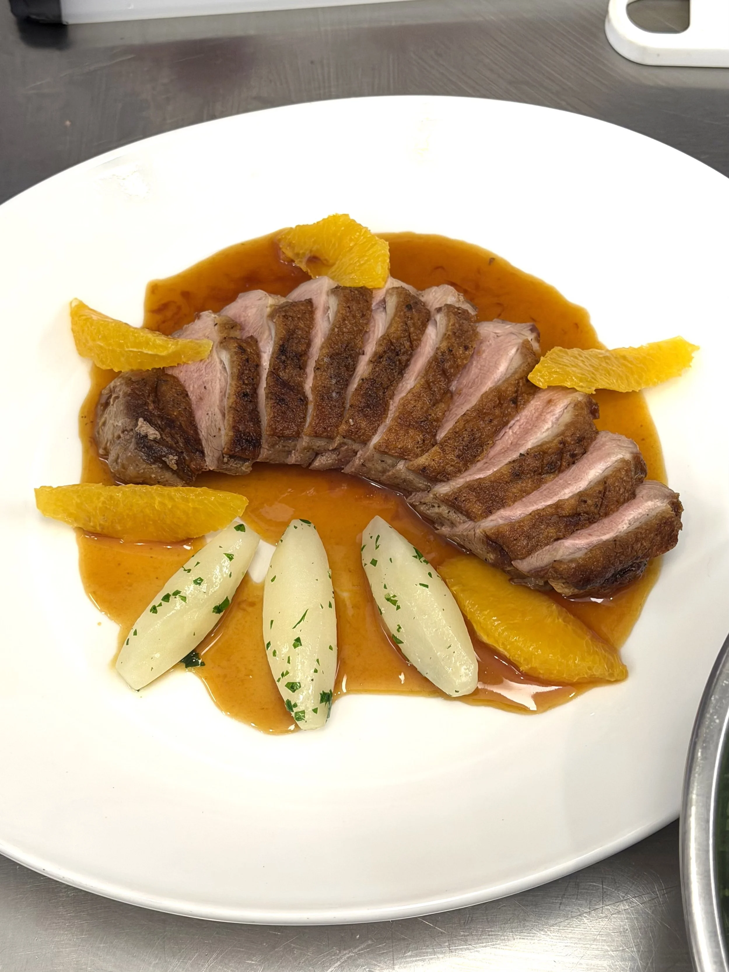 Sliced cooked meat with orange slices and a brown sauce on a white plate.