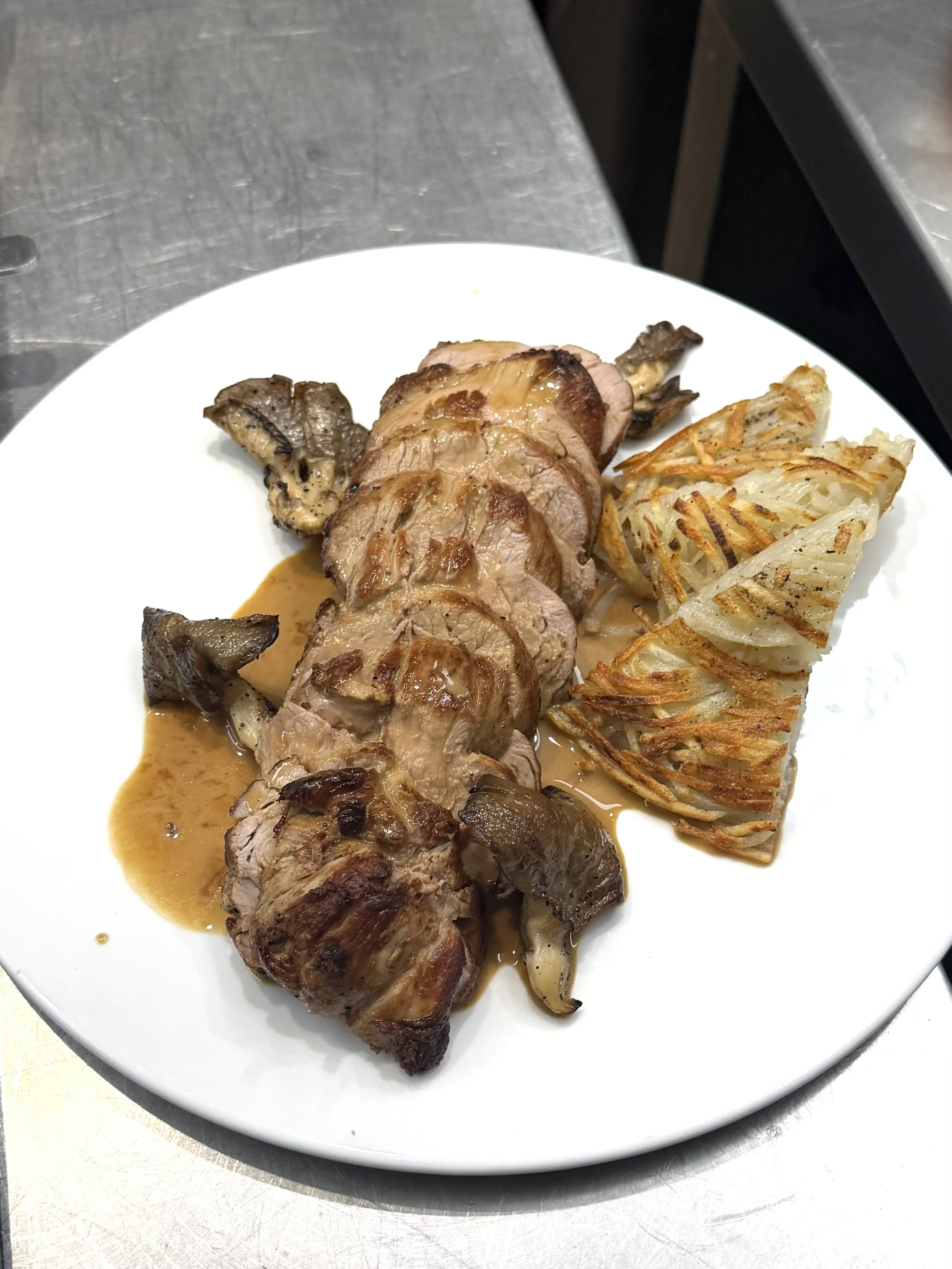 A white plate with sliced grilled meat, roasted mushrooms, and a potato rosti