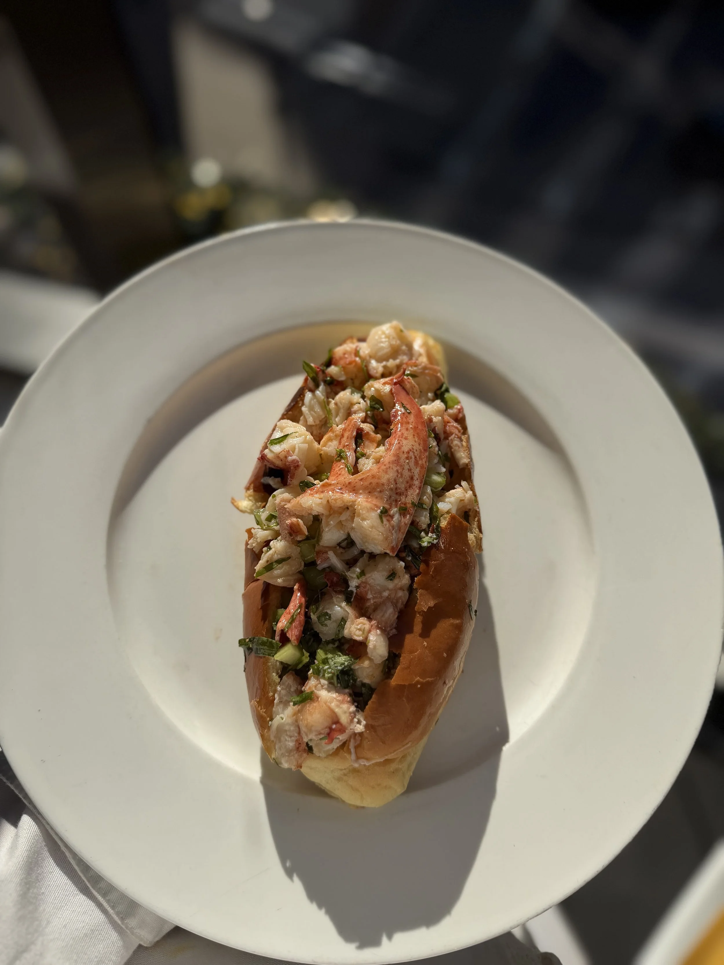 Lobster roll on a white plate with finely chopped herbs and seafood filling