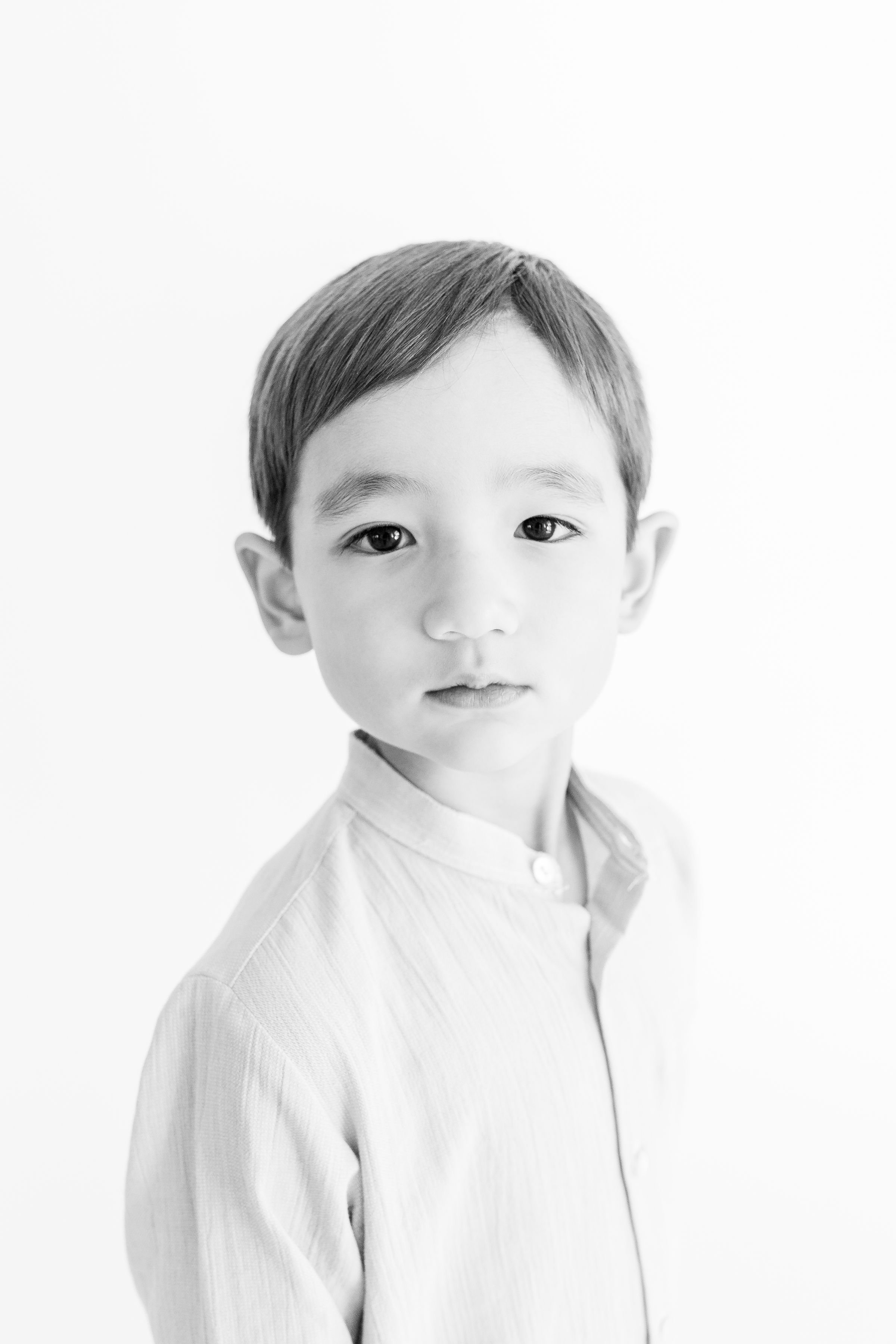 A young boy with short hair wearing a light-colored button-up shirt, looking directly at the camera against a plain white background.