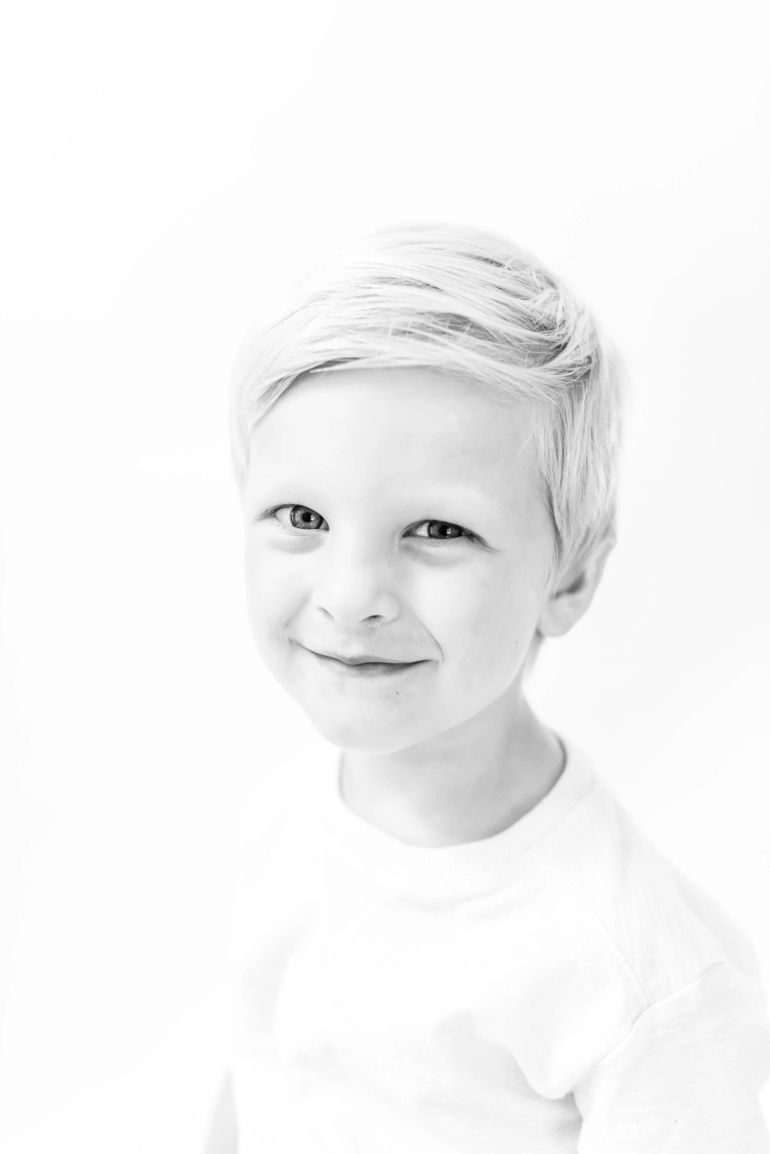Black and white portrait in heirloom style of a smiling young boy during a children's photography session documenting childhood personality.