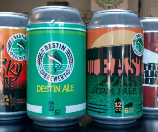 Three cans of craft beer from Destin Brewery, including Destin Ale with a green label, and  East Pass India Pale Ale with a black and orange label.