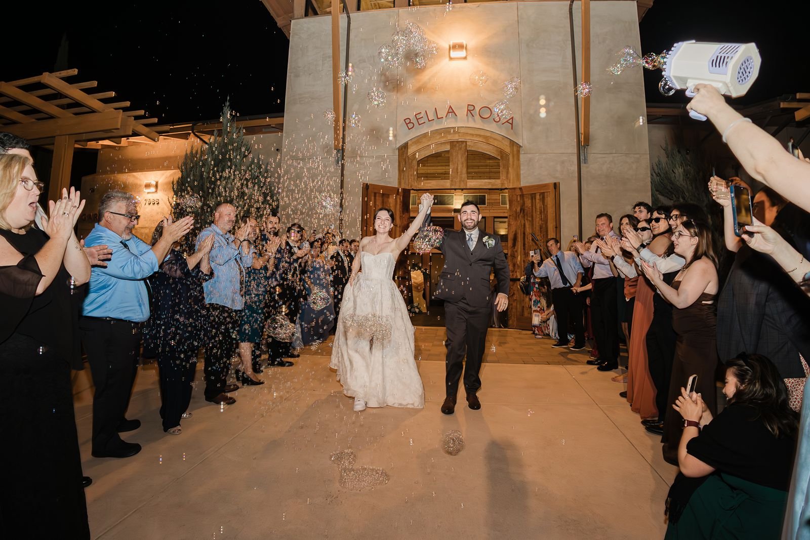 A couple exits the Casa Bella building surrounded by guests and bubbles at a Garre Winery wedding.