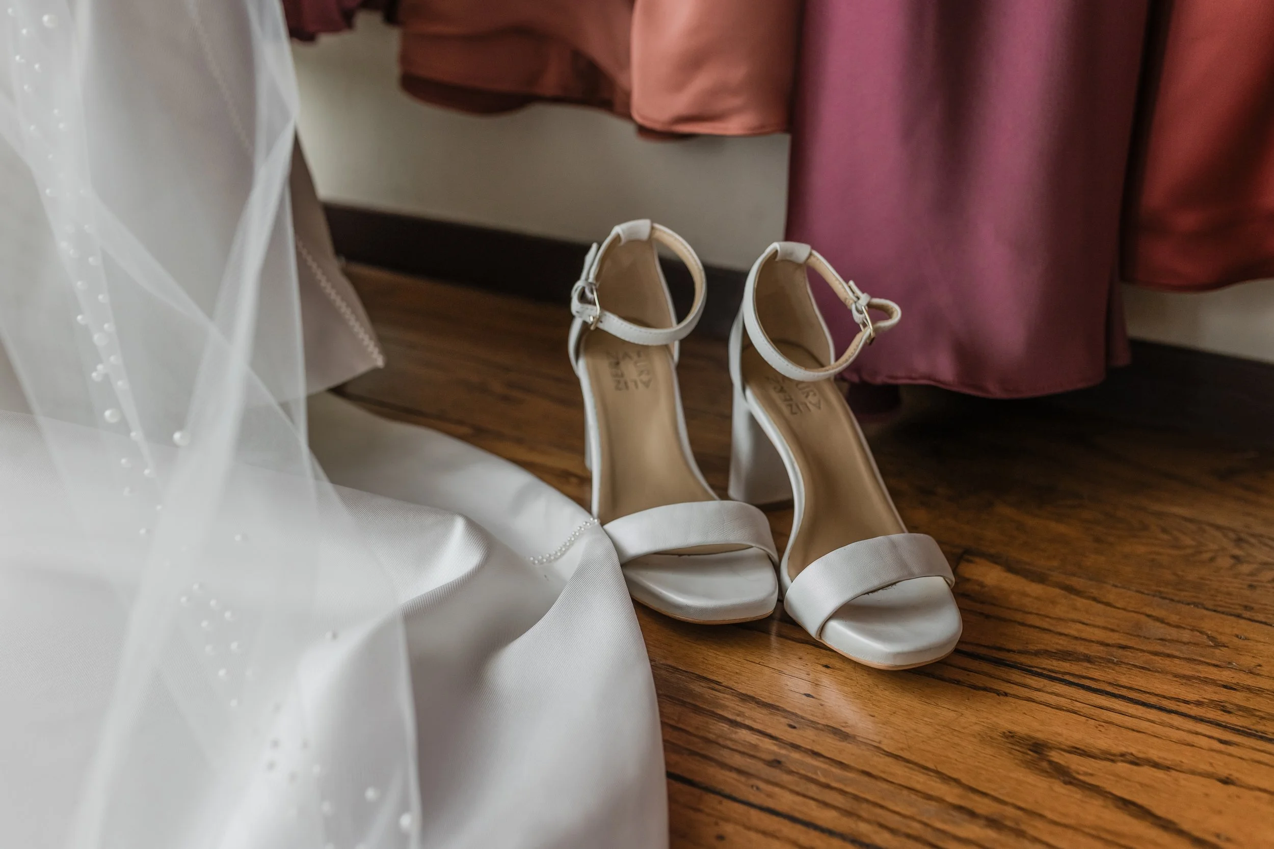 A pair of open toed white wedding heels next to a wedding dress.