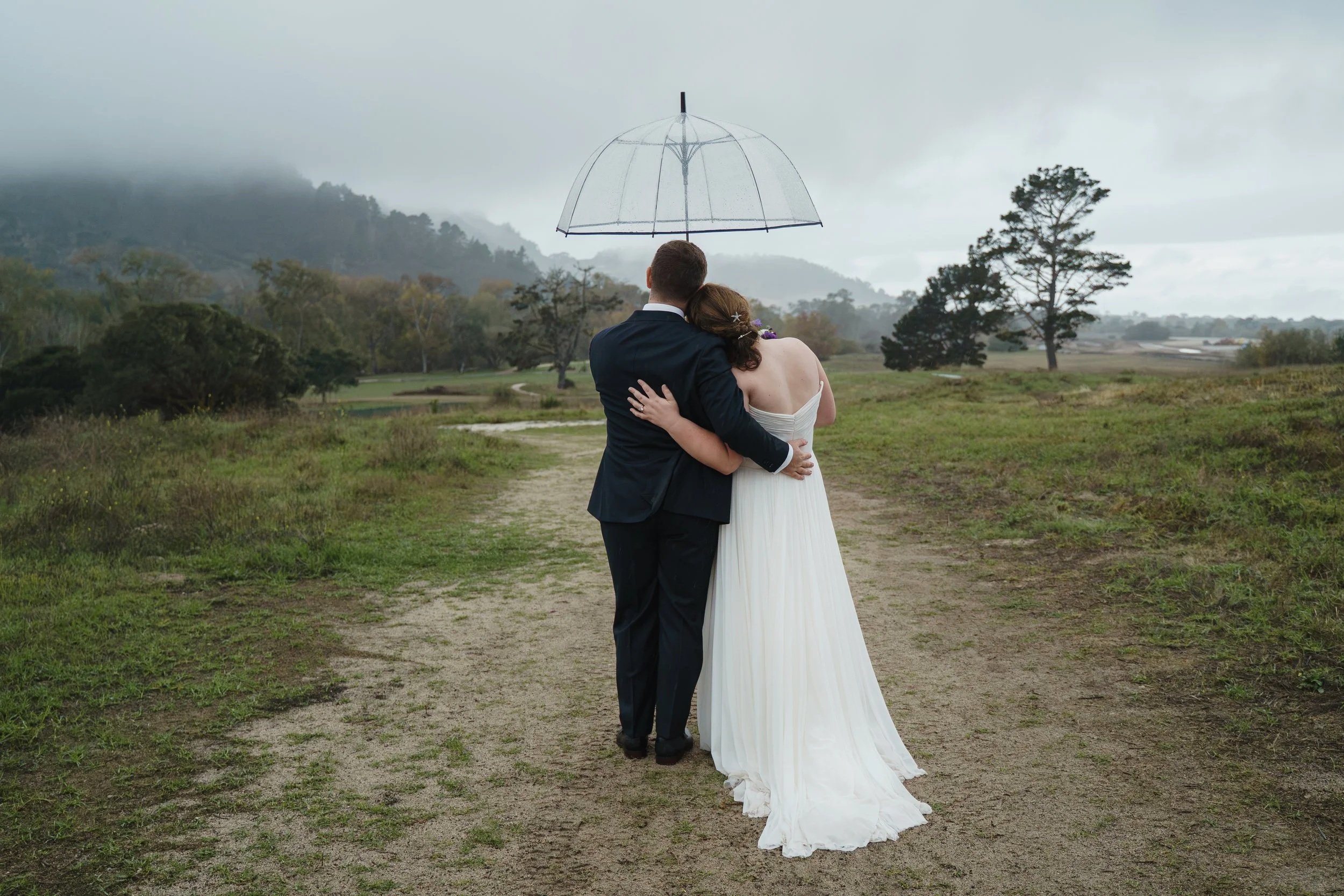 A married couple faces away and stands under an umbrella.