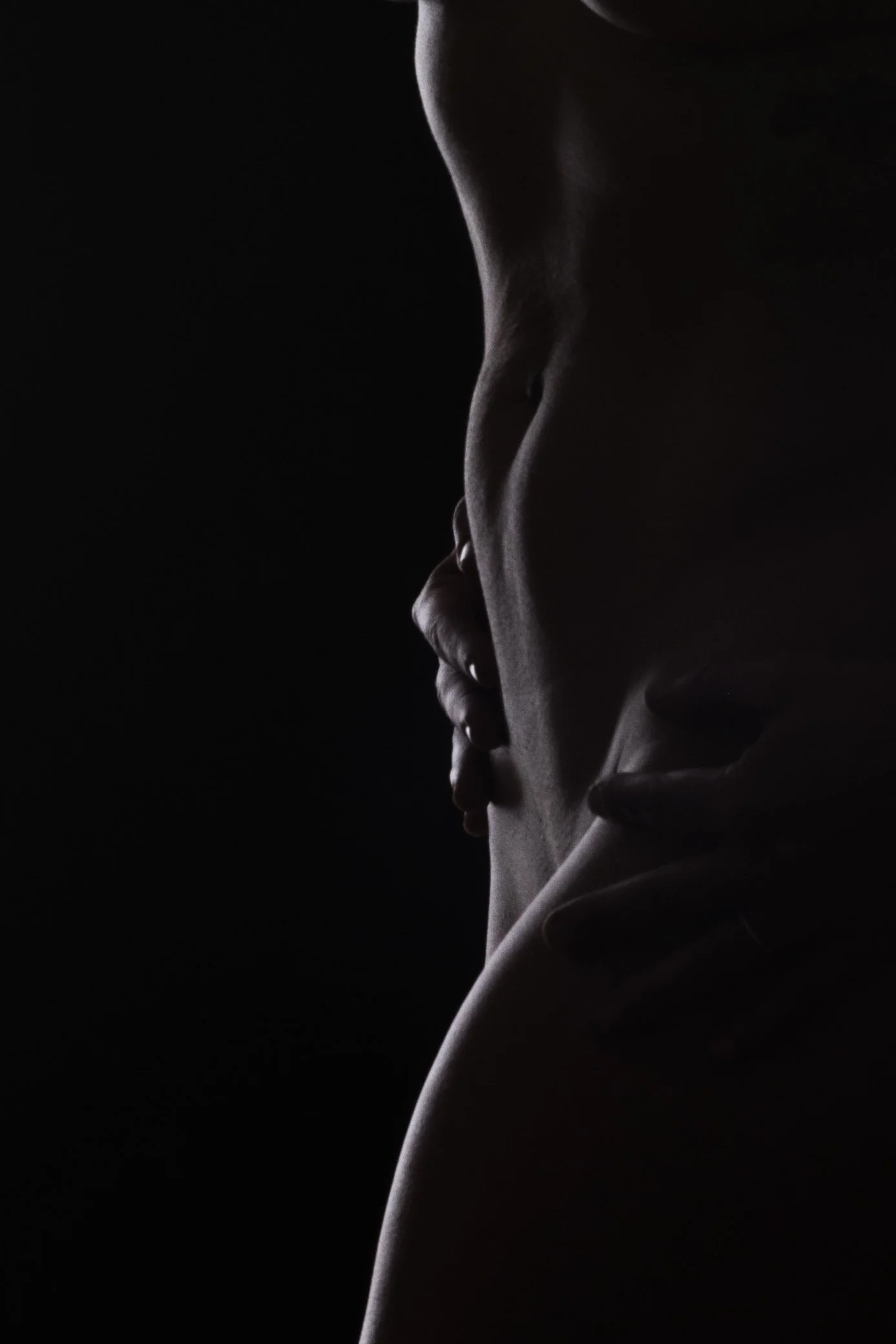Silhouette of a person's torso and hands in a dark setting with dramatic lighting.