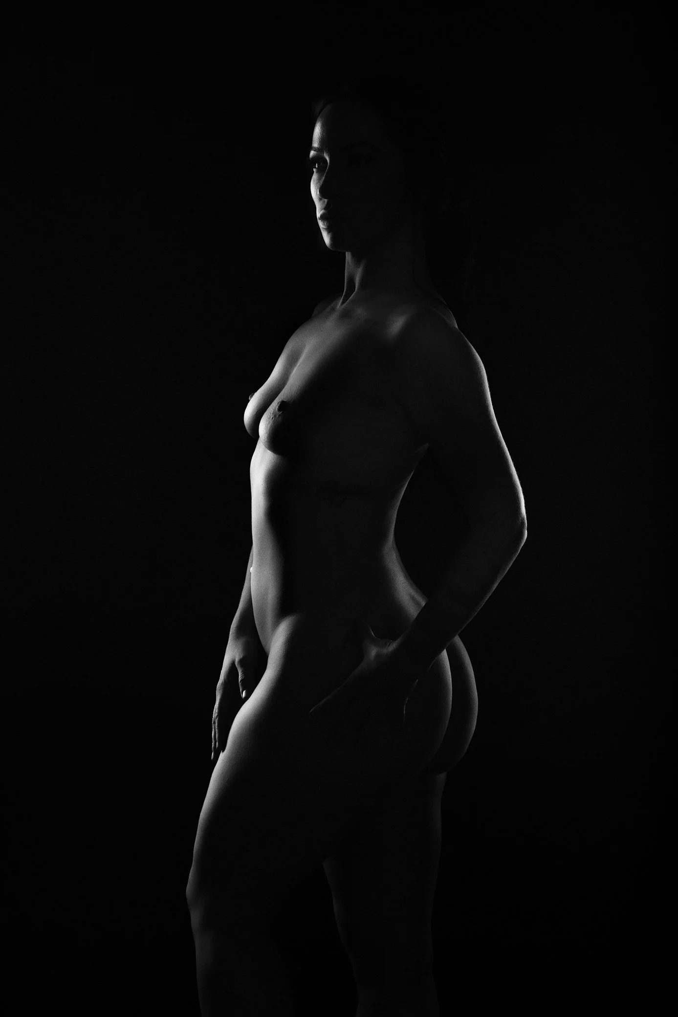 Black and white silhouette of a nude woman in side profile against a dark background.