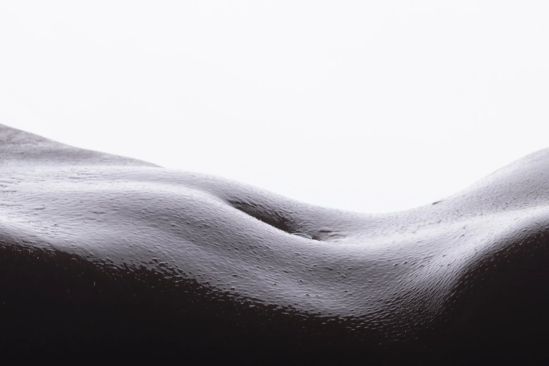 Close-up of a dark, wet, textured surface with smooth, rounded undulations, possibly a rock or geological formation.