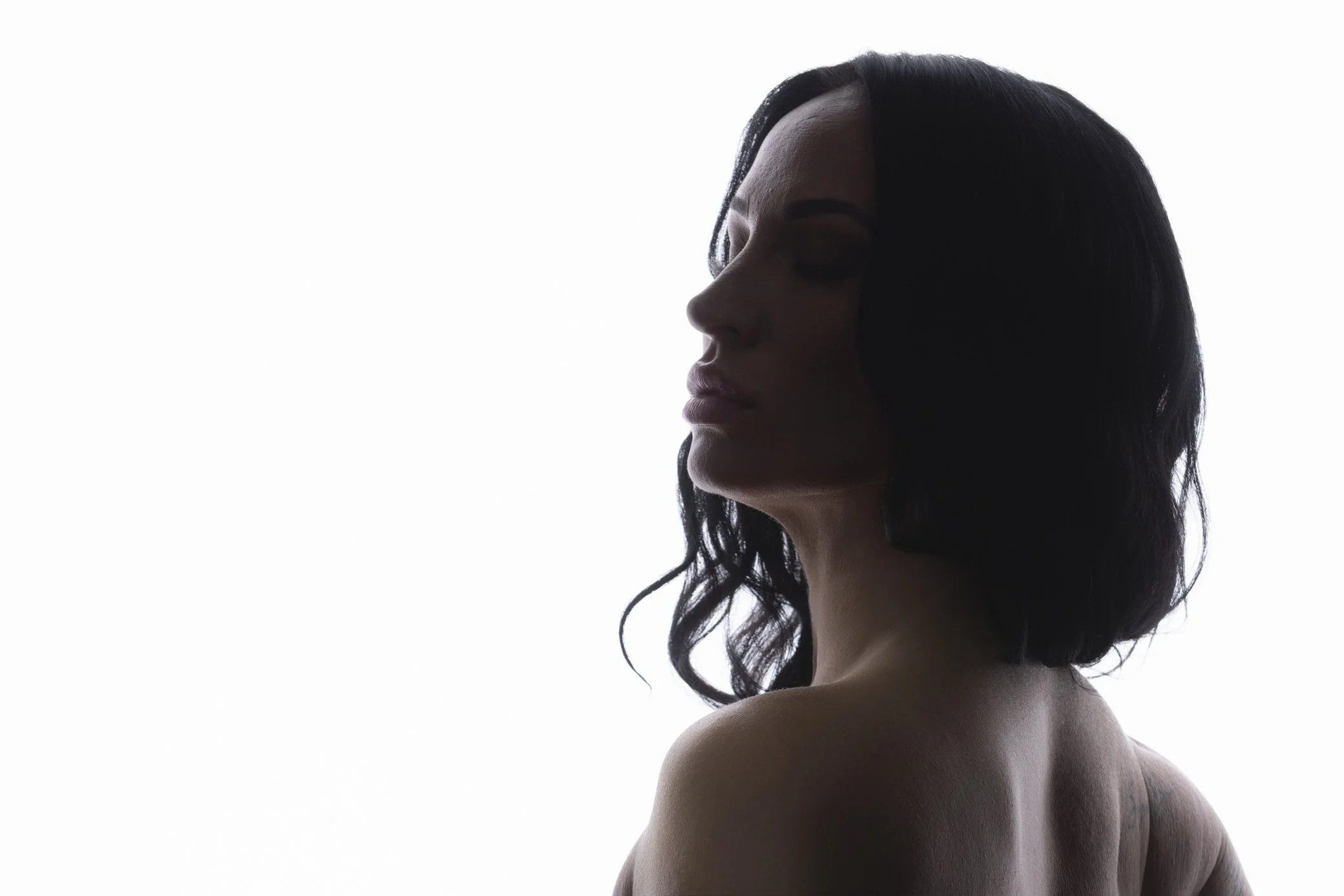 Silhouette of a woman with dark hair, her head turned sideways, against a plain white background, showing her shoulder and part of her back.