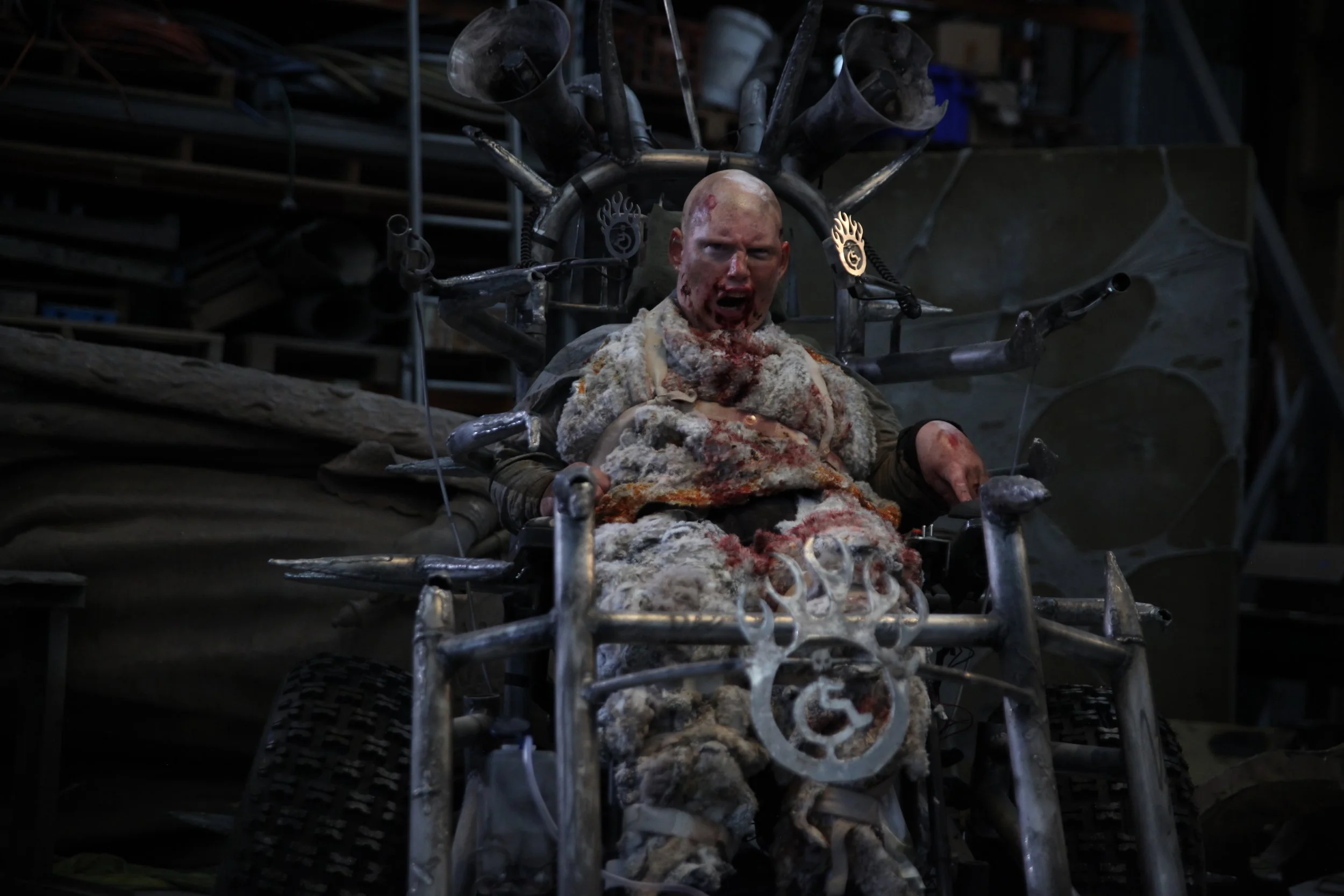 I'm in my apocalyptic wheelchair, fitted with large rusty spikes and microphones. I'm wearing filthy fur with dried blood incrusted. I'm growling, with blood around my mouth.