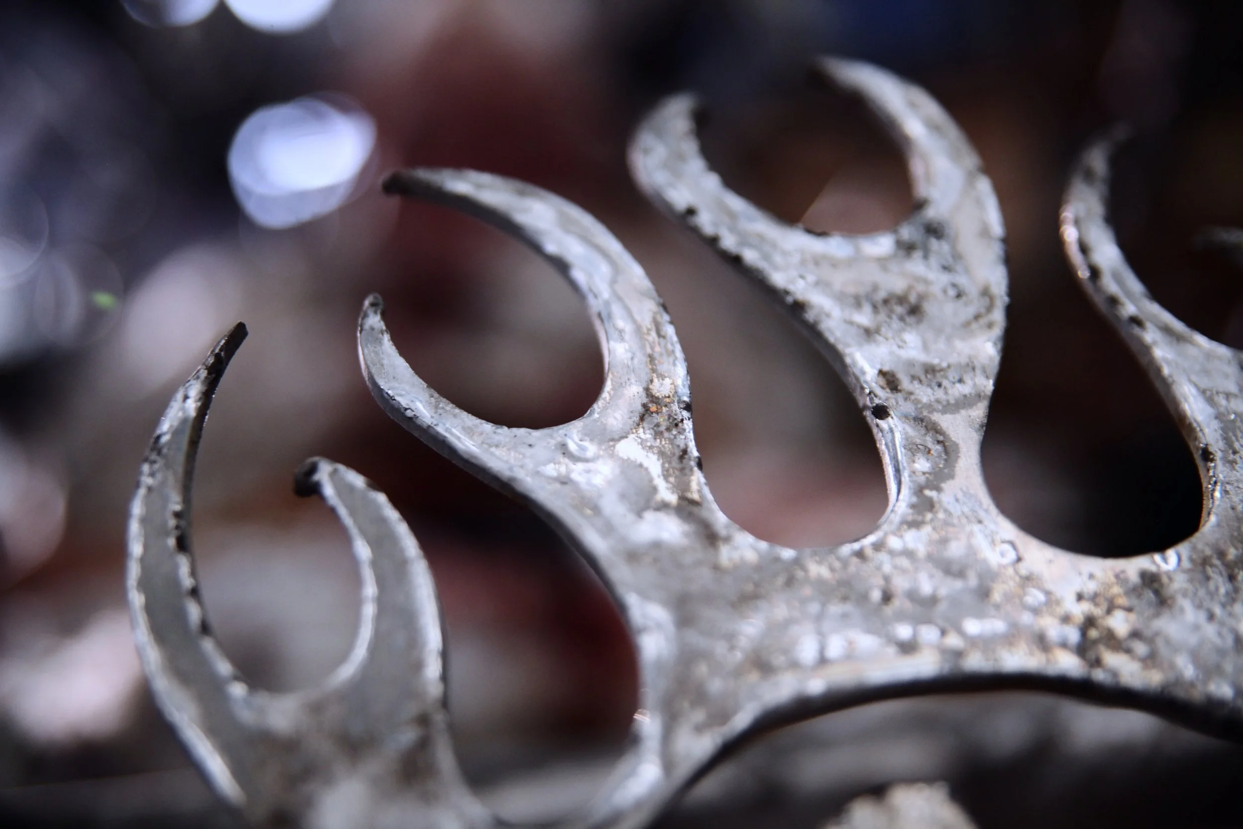 A close up of sharp metal flames which are decaying slightly, with a blurred background.