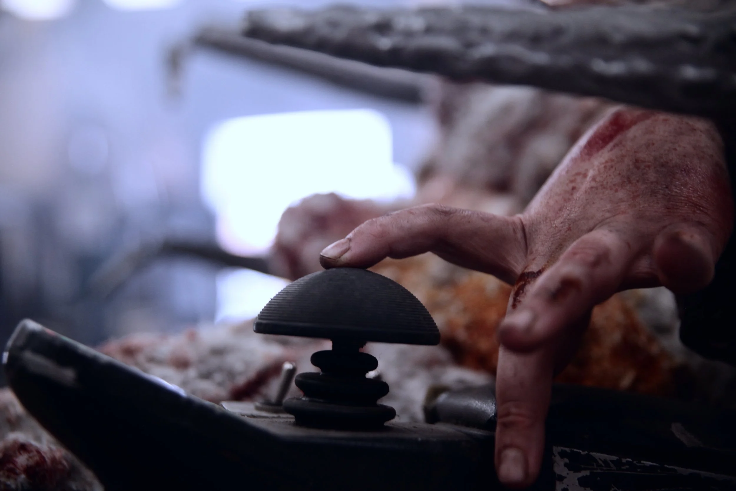 Close up of my finger on the controller of my power wheelchair as if I'm toying with the idea of moving forward. My finger is covered in dirt and dried blood.