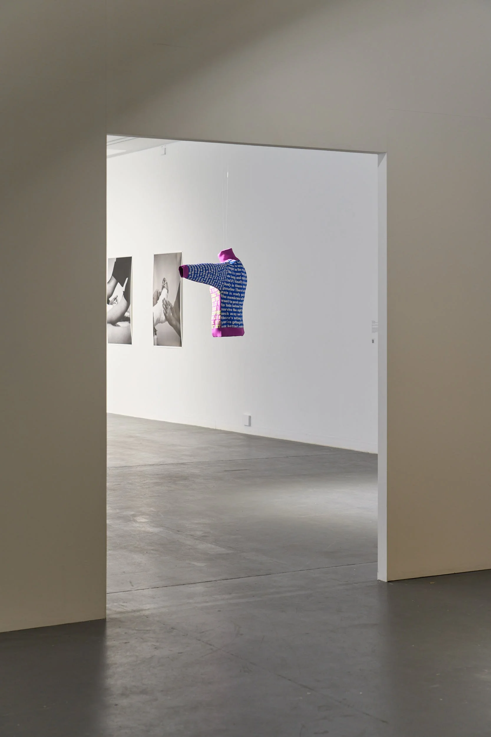 Makeda Duong’s work shown from inside a doorway. “Cradle the inspiration it will leave you writhing on the floor.” Sophie Cassar’s black and white photographs can be seen in the background.