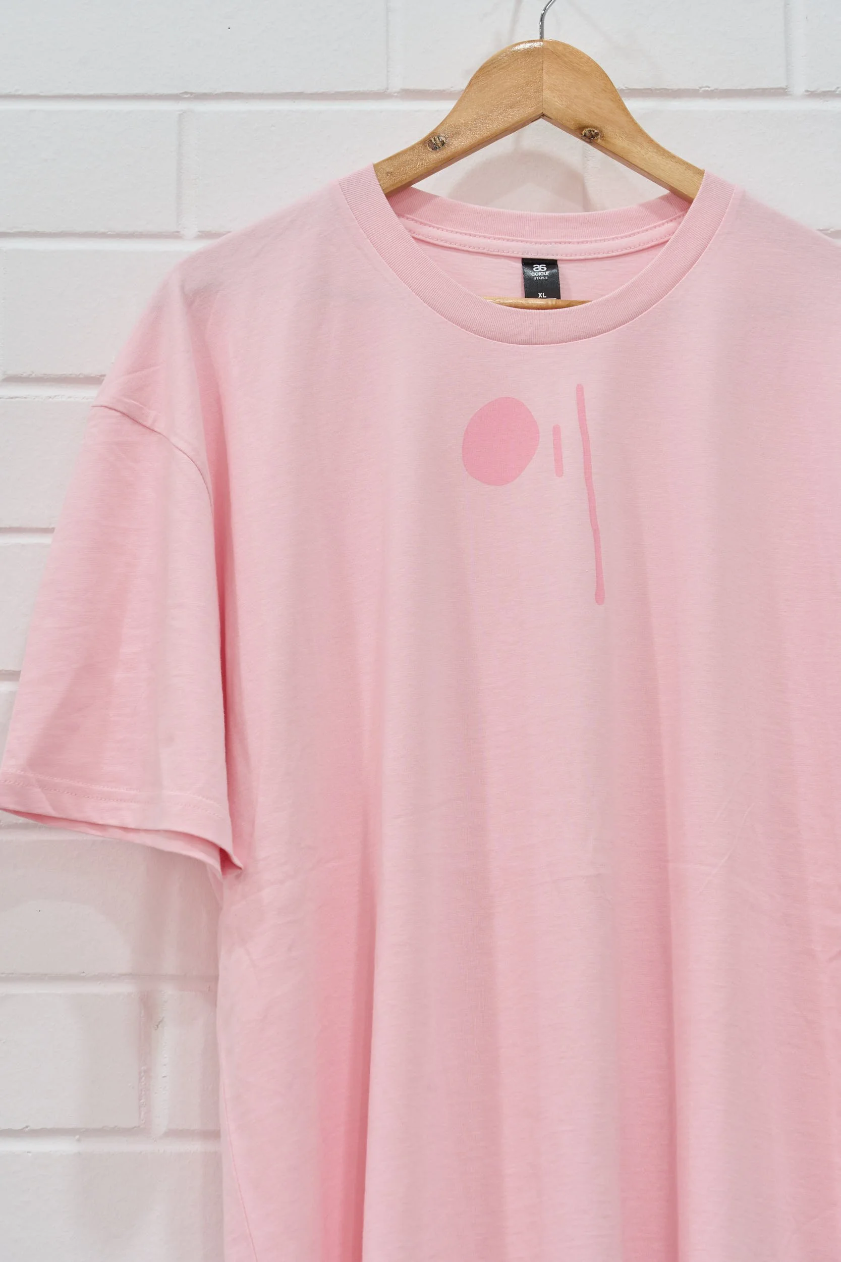 A close up image of a pale pink t-shirt with a drool graphic in a darker pink tone printed on the front.
