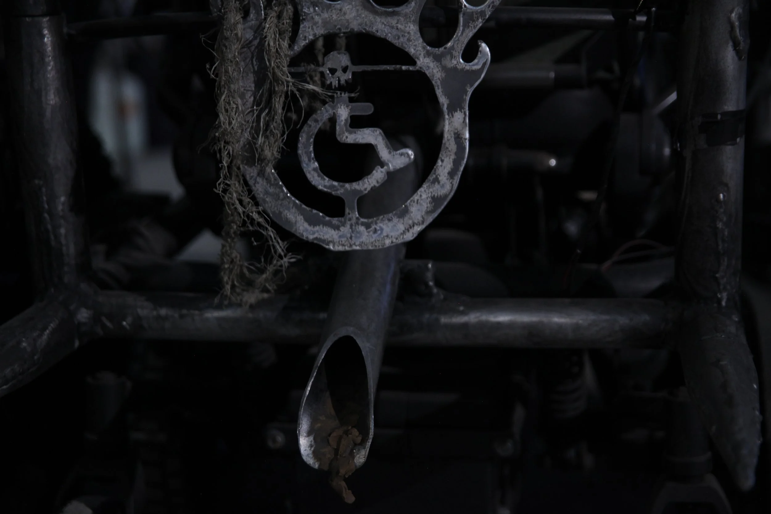 My symbol of a wheelchair has been cut out of tarnished metal. Below is an exhaust pipe with poo coming out of it.