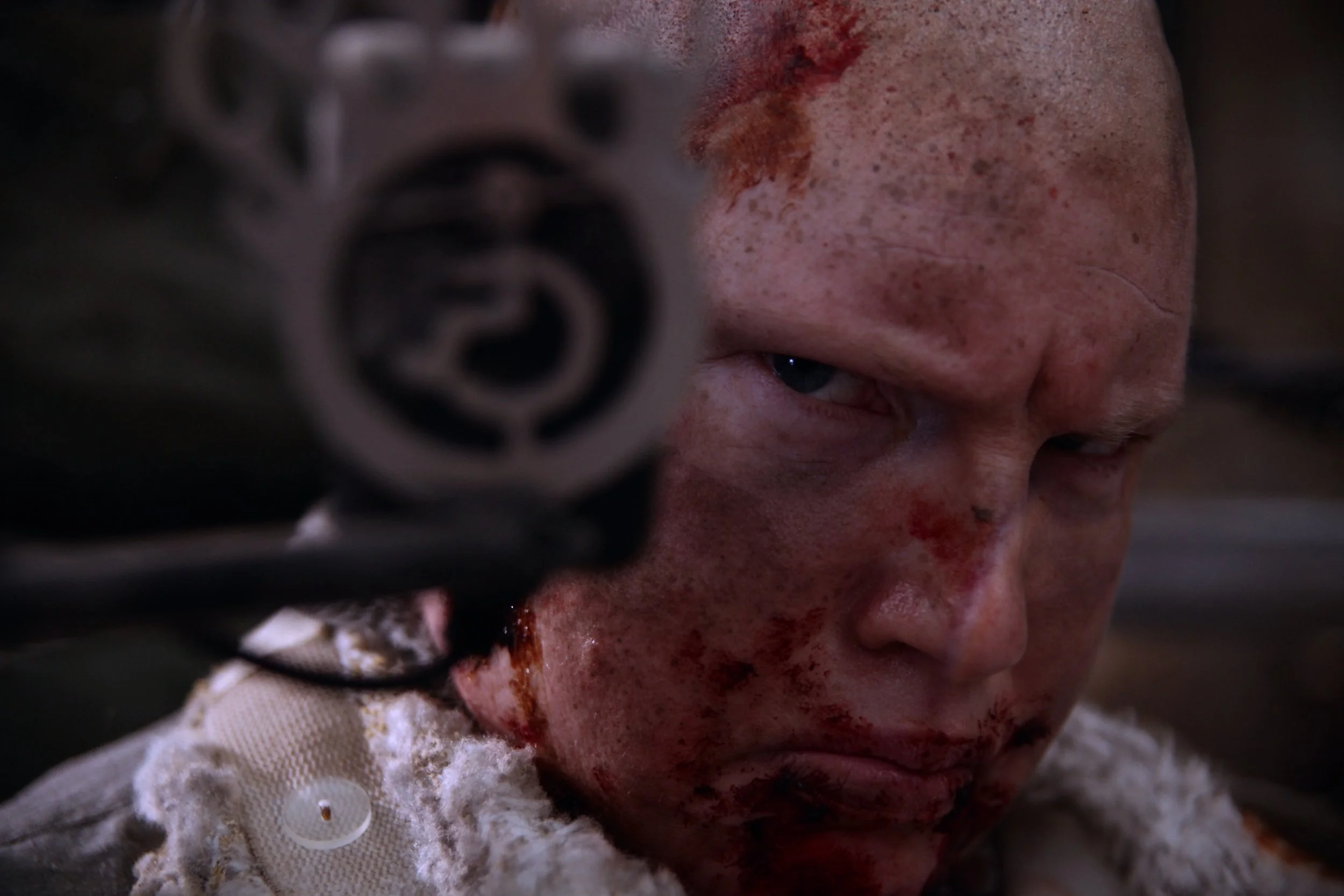 A close up of my filthy face making direct eye contact, My expression is serious and angry and my face is dirty, covered in sweat and dry blood.