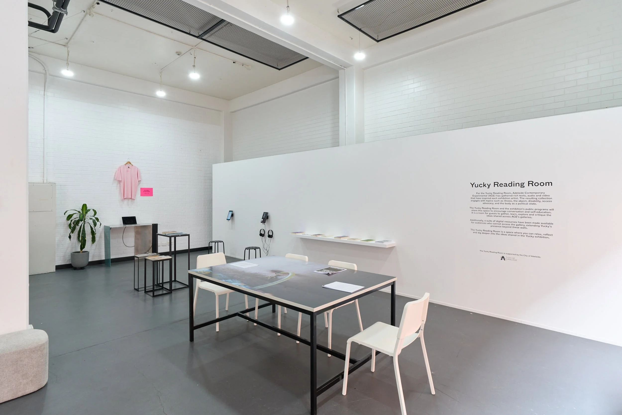 Full view of ‘Yucky reading room’ featuring texts, videos, images, and audio resources which are displayed for people to engage and interact with. A pink shirt hangs in the background.