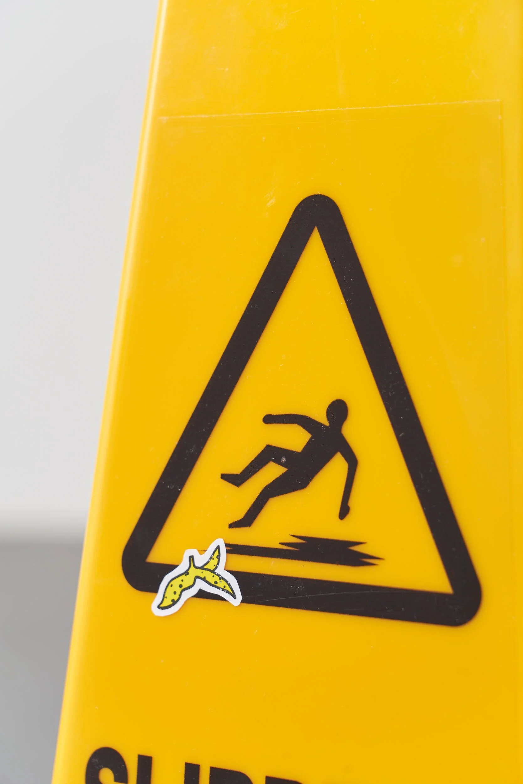 Close up image of the graphics on the yellow hazard sign. A person is shown slipping. There is a little banana peel sticker that has been added to the sign under the person’s feet.