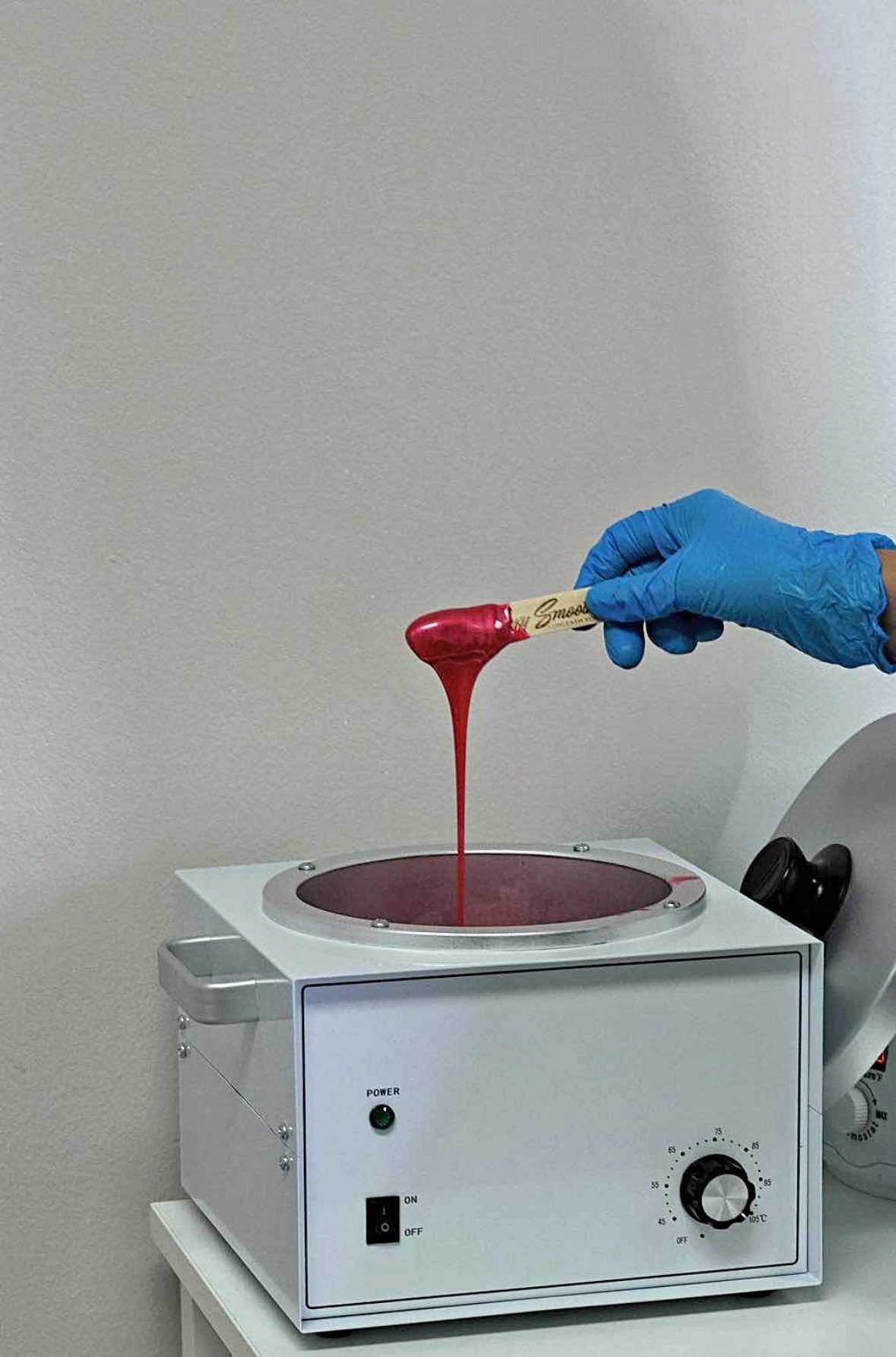 A gloved hand is holding a chocolate lollipop, pouring melted red chocolate into a heating machine.