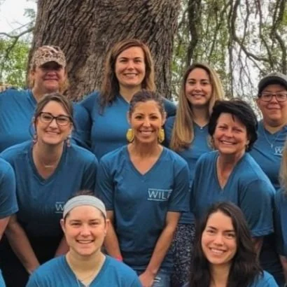 Group of women in matching blue shirts standing outdoors in front of a large tree.