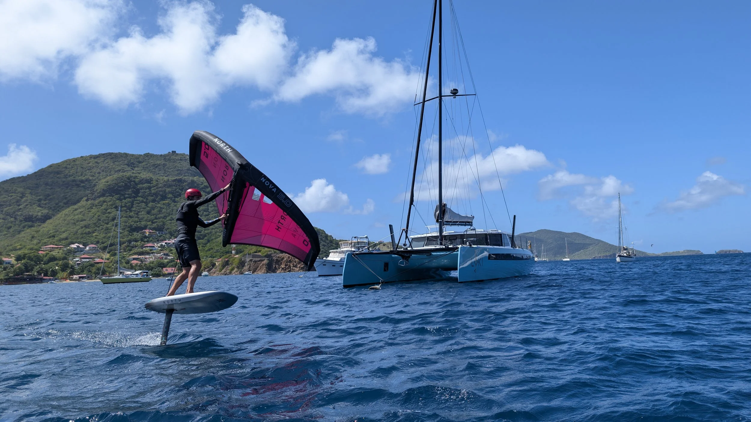 Person kiteboarding on turquoise water near a small island under a partly cloudy sky.