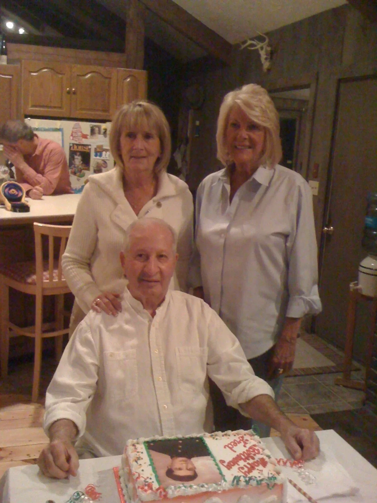 Two women standing and a man sitting in front of them, all three looking at the camera and smiling.