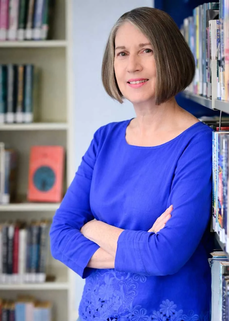 Photo of historical fiction author Elisa M. Speranza in a blue shirt in a library with books.