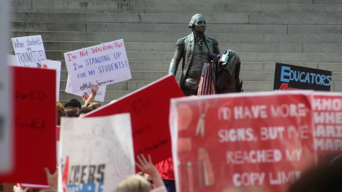 George Washington peers over posters at the #RedForEd demonstration.
