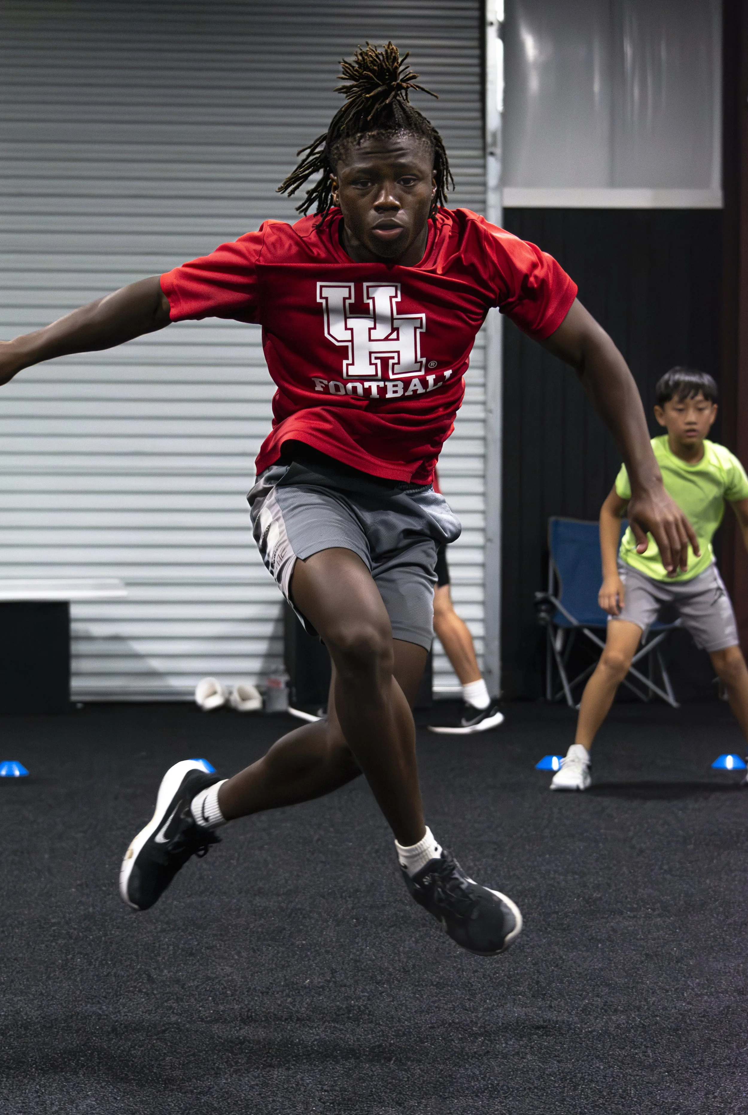 Football player in a red jersey lunging during an indoor training drill, with teammates in the background