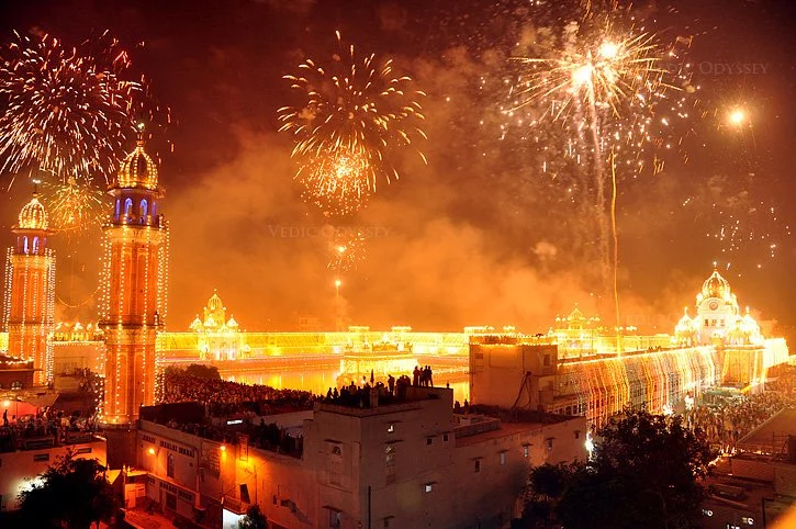 Fireworks exploding over a lit-up palace with a large crowd gathered below during nighttime.