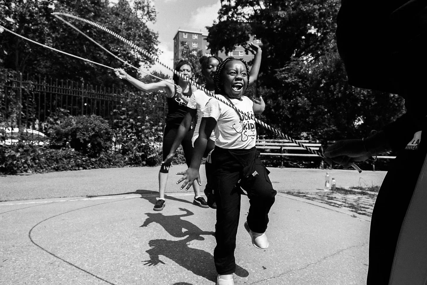 Black girls eith braided hair double-dutching in the city. Black and white photo.