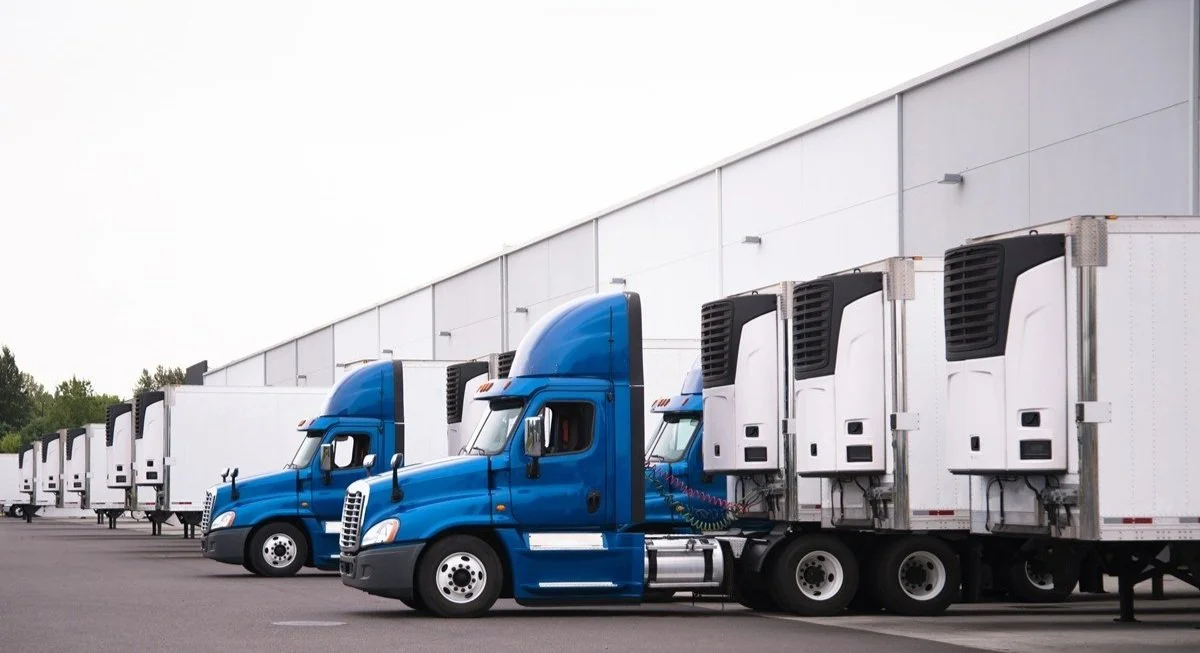 Line of blue semi trucks with refrigerated trailers parked in a lot.