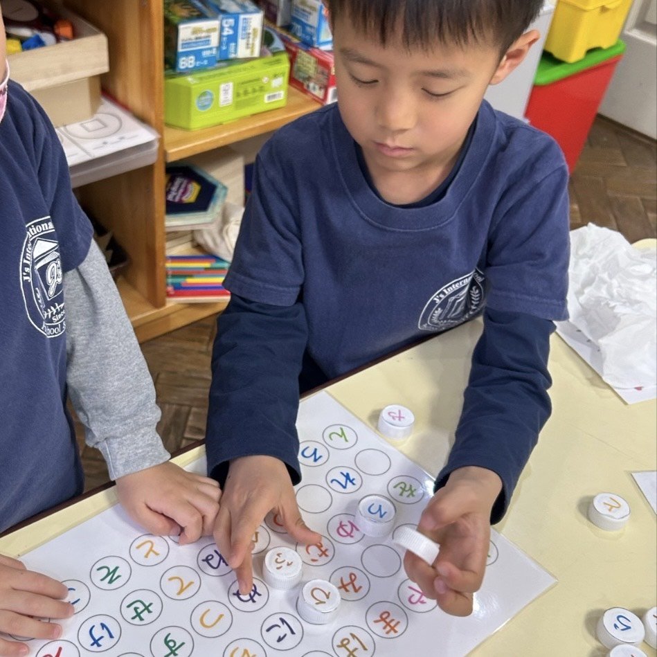 Two children engaged in a counting activity using numbered bottle caps and a grid with colored numbers on a table.