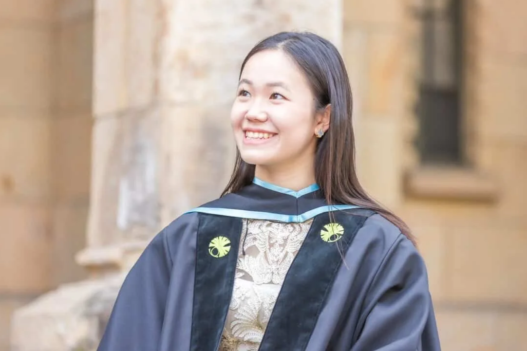 Young woman in graduation gown smiling outdoors.