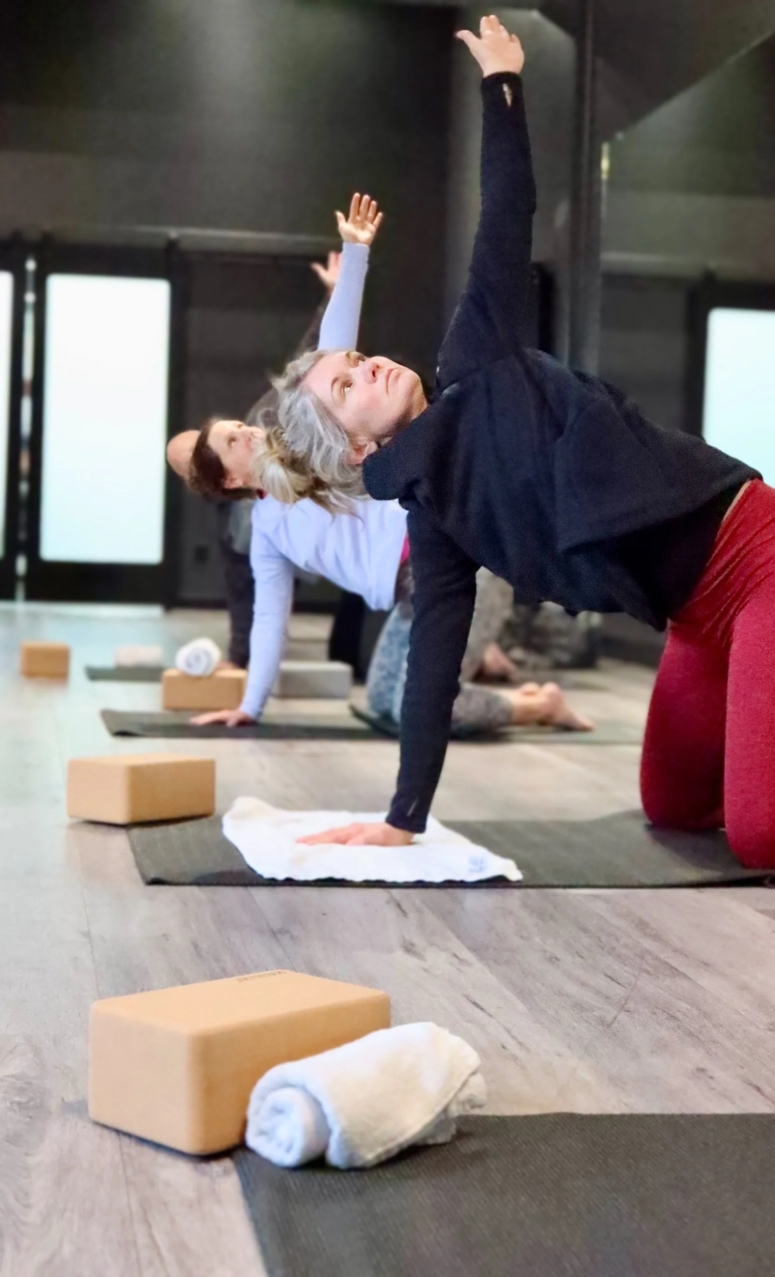 People practicing yoga in a studio, in a pose on mats, with blocks and towels nearby.
