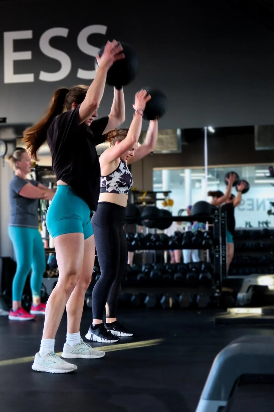 Women doing a workout with medicine balls in a gym.