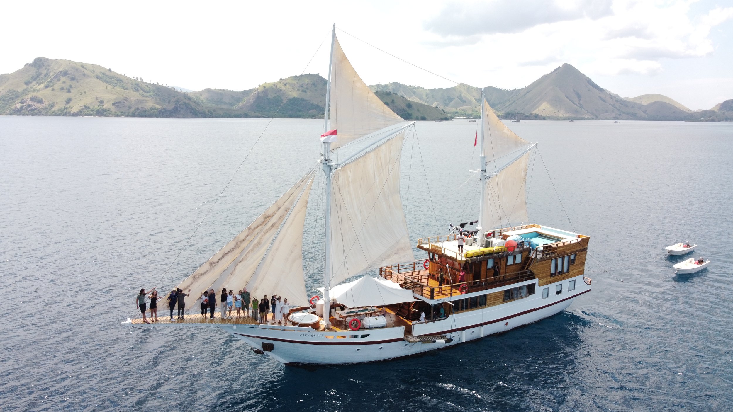 A sailboat with people on board sailing on a body of water with hills in the background.