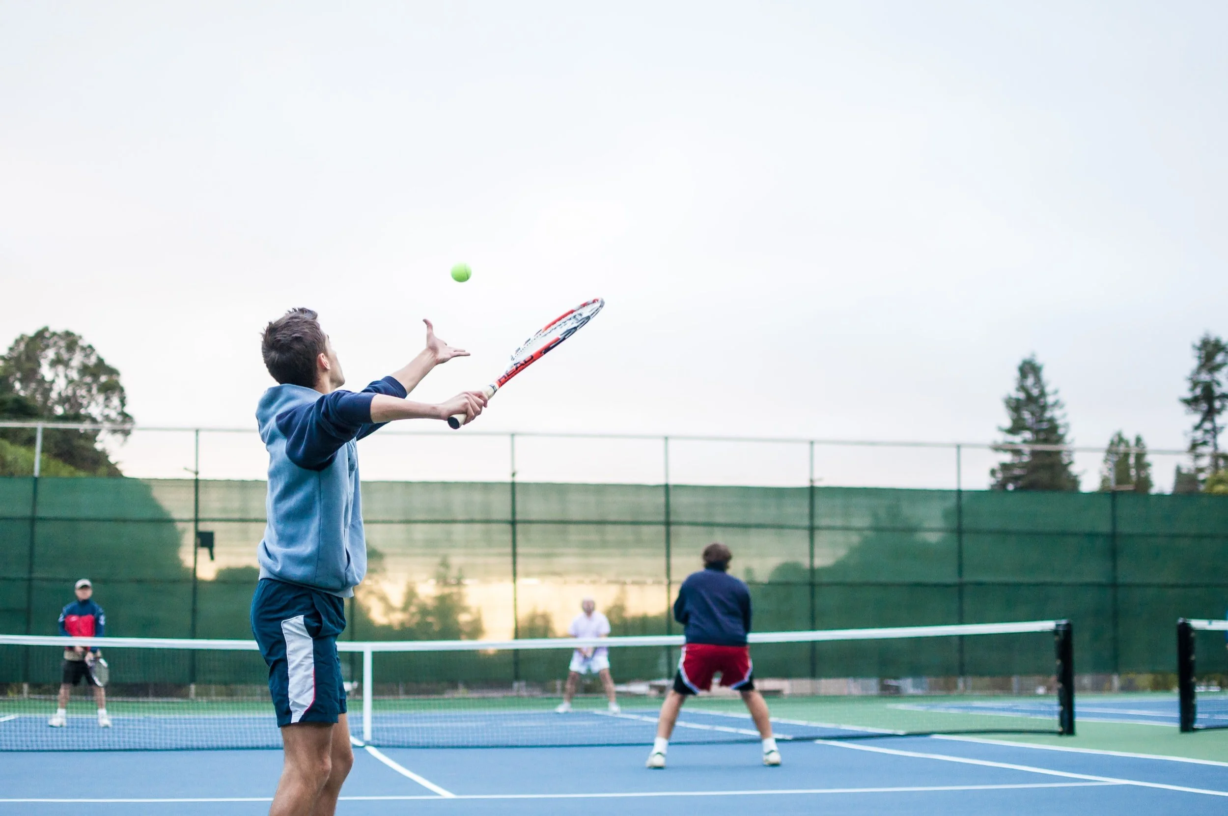 A group of people playing pickleball on an outdoor court.