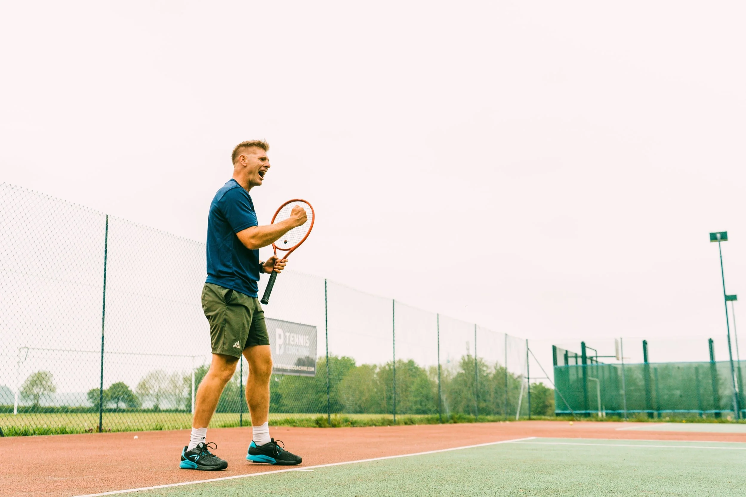 A man on a tennis court celebrating with a fist pump while holding a tennis racket.