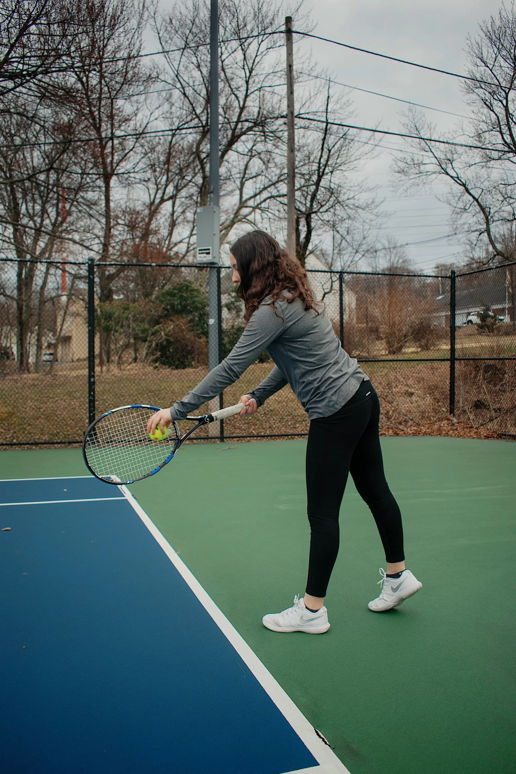 A woman playing tennis on an outdoor court, about to hit a tennis ball with her racket.