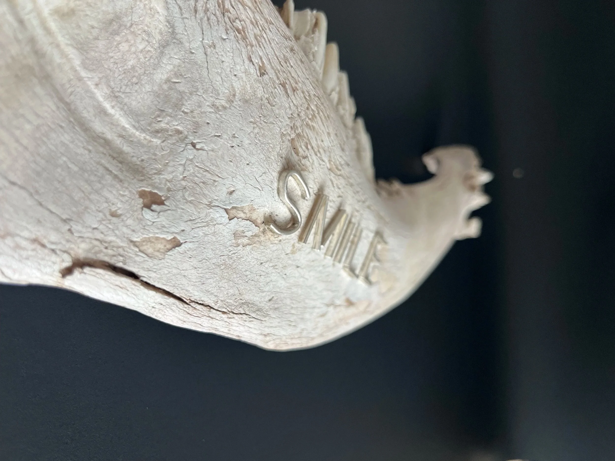 Close-up of a weathered, off-white sculpture with the partially visible word 'SMILE' engraved on it, against a black background.