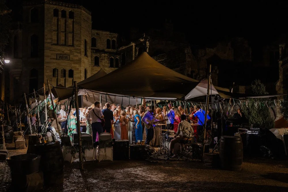 An evenning wedding reception under a marquee with Guys Cliffe House ruins in the background at night