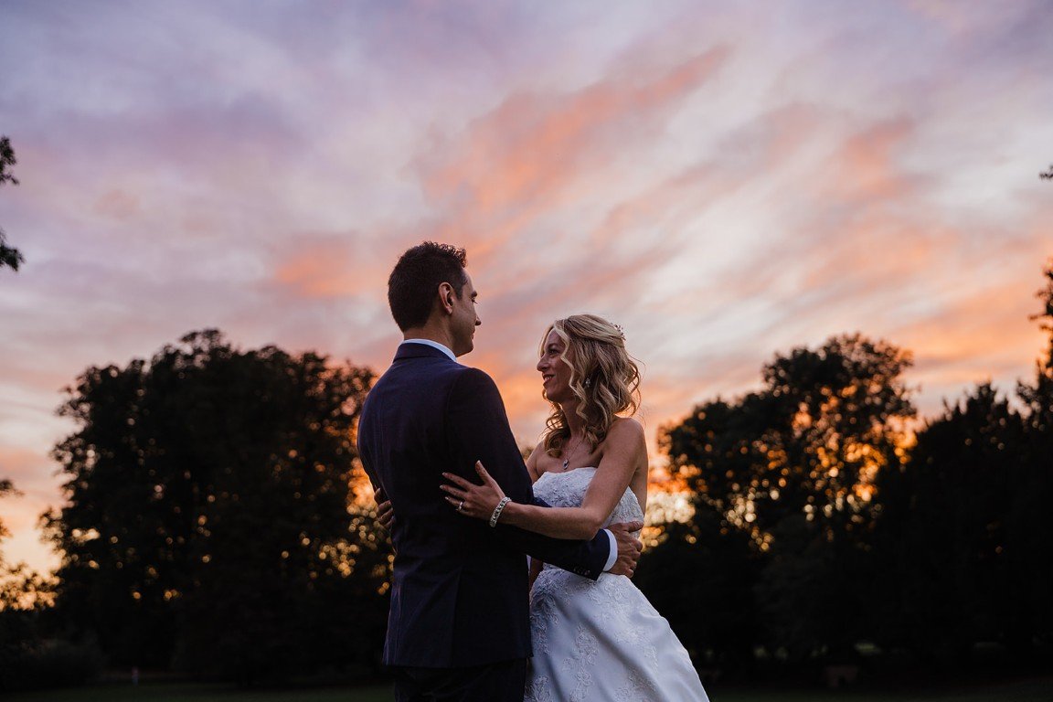 A couple in wedding attire sharing a moment outdoors at sunset with trees in the background.