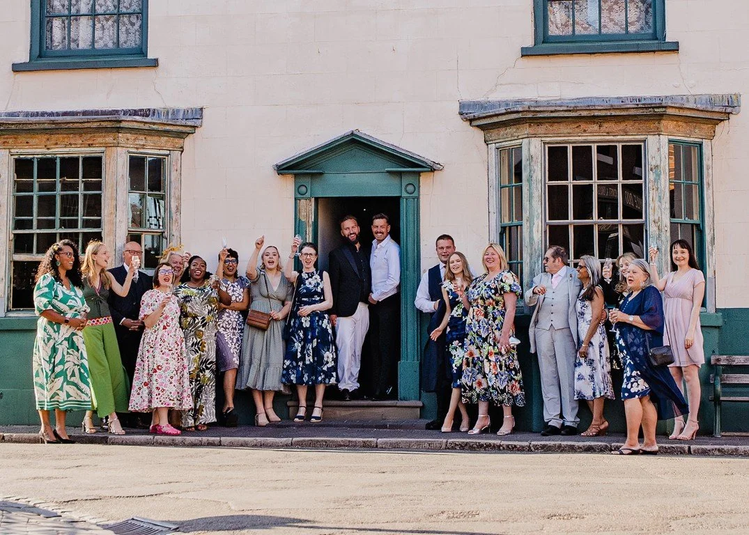 Group of people standing outside a building, celebrating, with two men in the center holding each other and smiling.